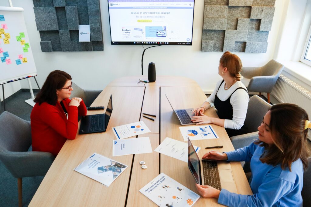 Three women collaborating in a modern office with laptops and presentation materials.